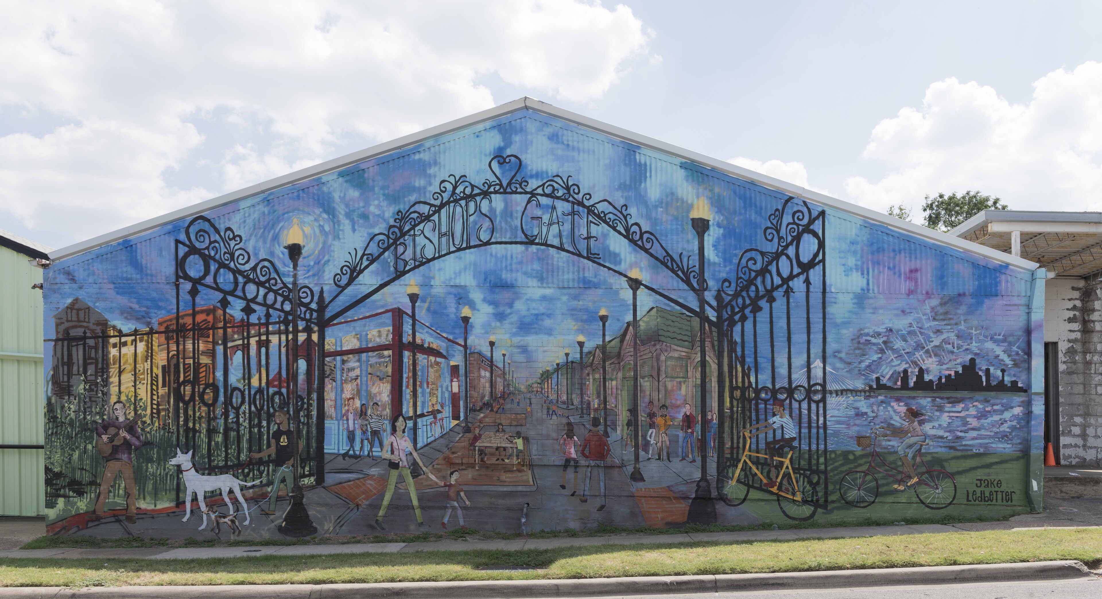 A large painted mural on the gable wall of a building in the Bishop Arts District, showing a wrought-iron gate arch reading "Bishop's Gate" over a street scene of walkers, a cyclist, and storefronts under a swirling blue sky.